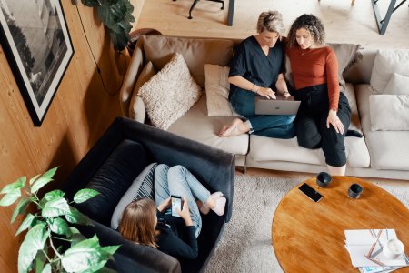Foto av tre personer som sitter i en stue og ser på mobil og pc. 