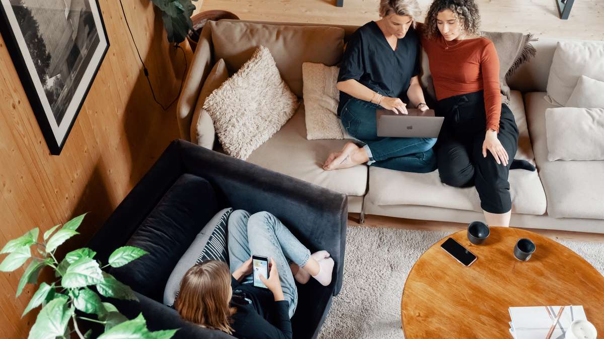 Foto av tre personer som sitter i en stue og ser på mobil og pc. 